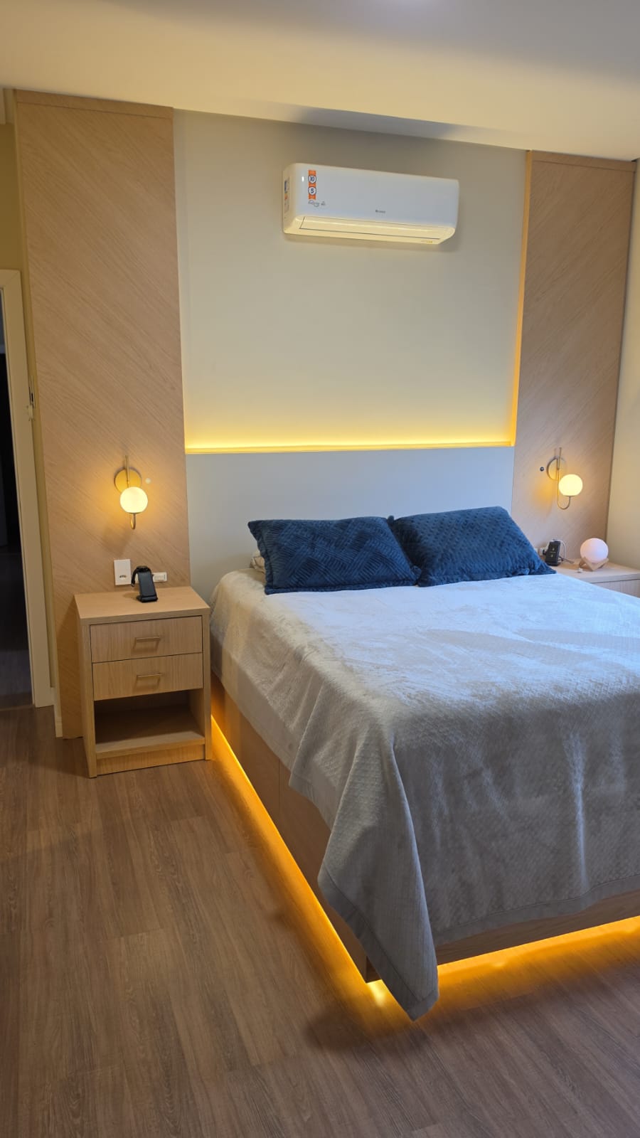 Quarto de casal com cabeceira ripada e iluminação indireta